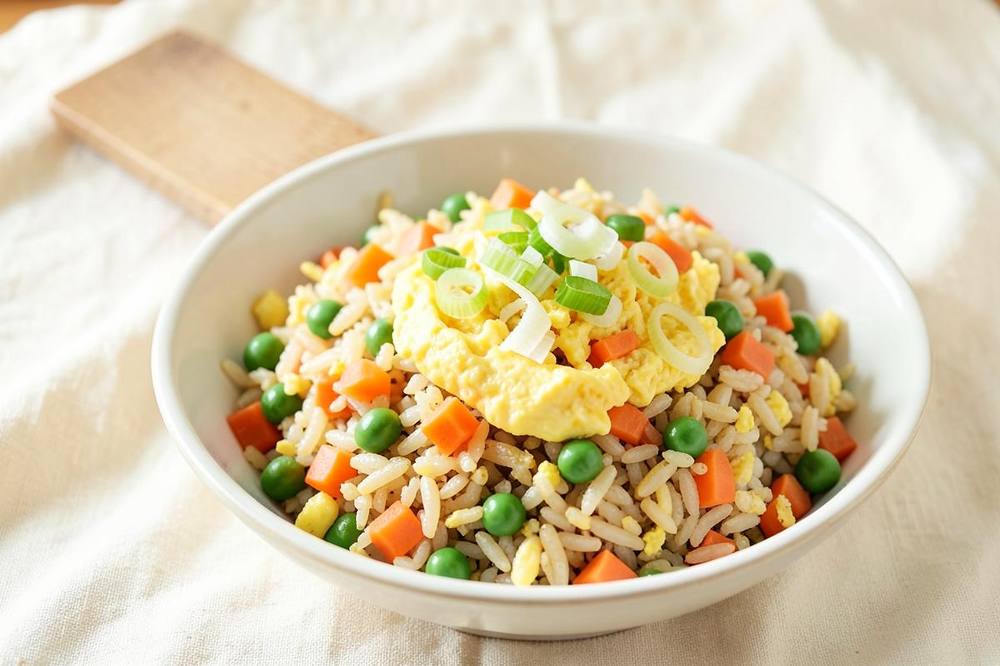 Bowl of egg fried rice with peas, diced carrot, scrambled egg and sliced spring onions
